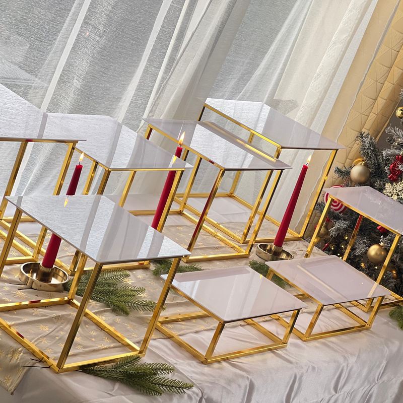 Présentoirs cubes dorés à plateau blanc, bougies rouges et branches de sapin sur une table de Noël