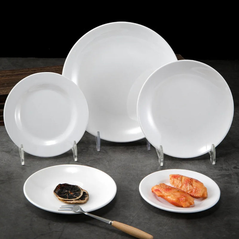 Trois assiettes blanches de tailles différentes et deux assiettes garnies sur une table sombre