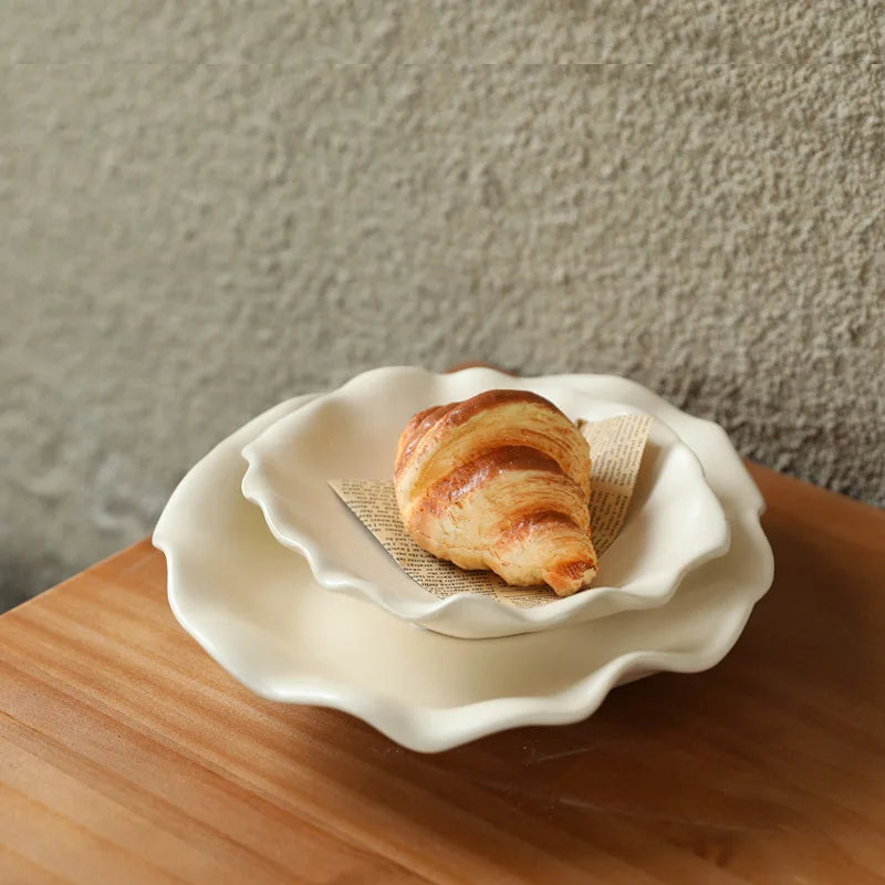 Plats en céramique crème à bord ondulé superposés, avec un croissant dans le plus petit