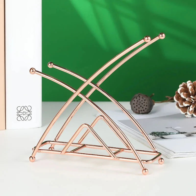 Porte-serviettes rose cuivré à branches croisées, variante Rose Forme X, posé devant un livre blanc et une pomme de pin