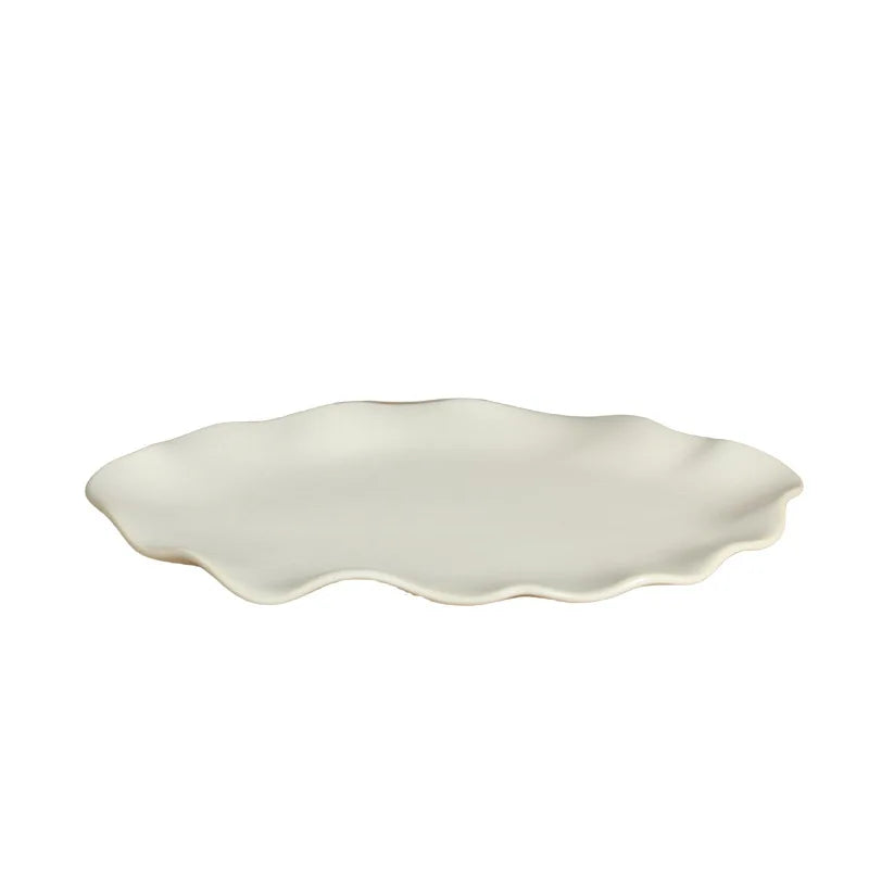 Grand plat en céramique crème à bord ondulé vu de profil sur fond blanc