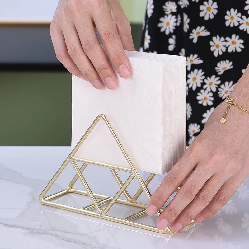 Porte-serviettes triangulaire en fil doré avec une pile de serviettes blanches, mains posant une serviette