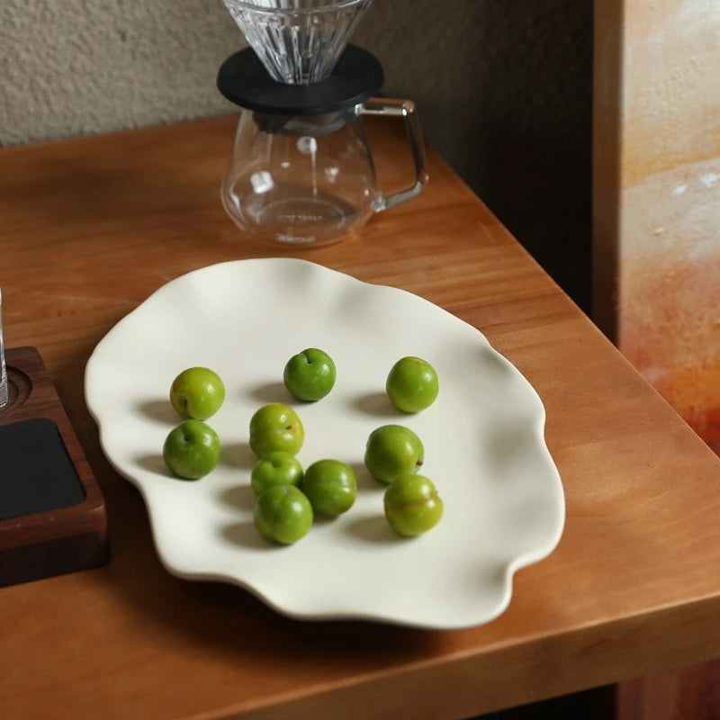 Grand plat en céramique crème à bord ondulé garni de prunes vertes sur une table en bois