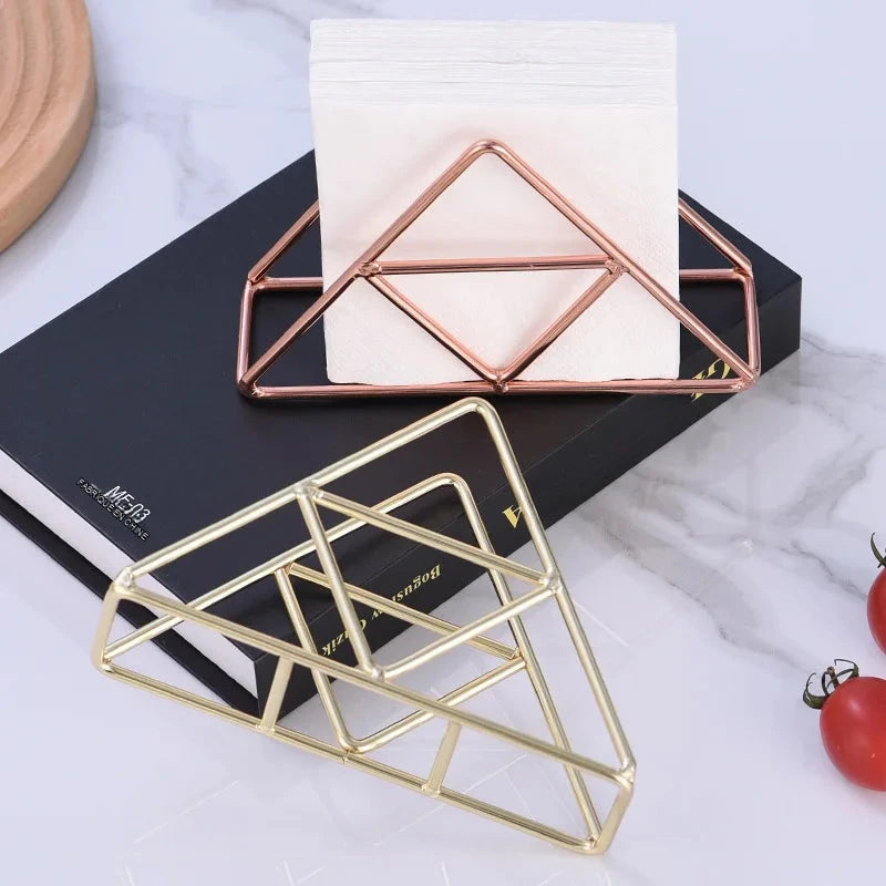 Deux porte-serviettes triangulaires en fil métallique, l'un rose cuivré, l'autre doré, posés sur un livre noir