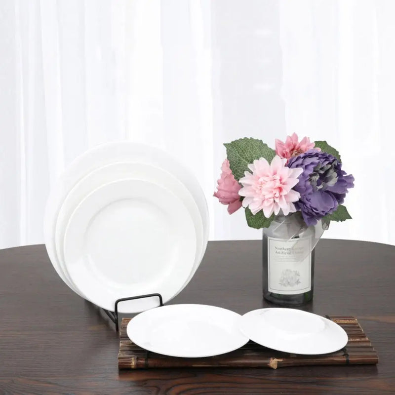 Assiettes blanches rondes sur un support, à côté d'un vase de fleurs