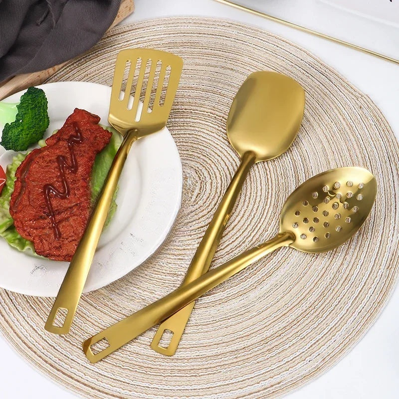 Spatule ajourée, pelle et cuillère perforée dorées posées près d'une assiette de viande et de brocolis