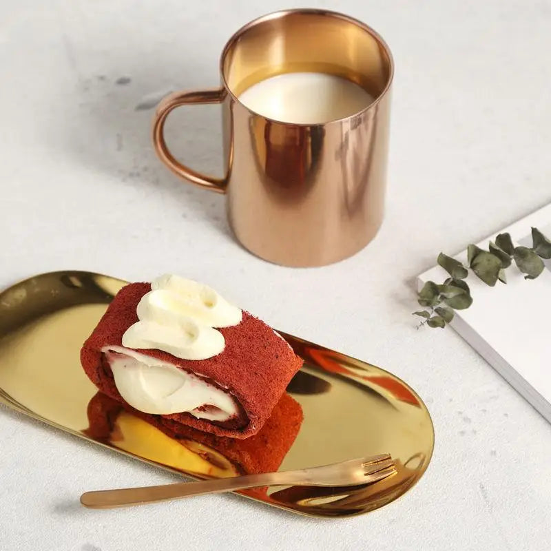 Plateau ovale doré portant une part de gâteau roulé et une fourchette, à côté d'une tasse en cuivre