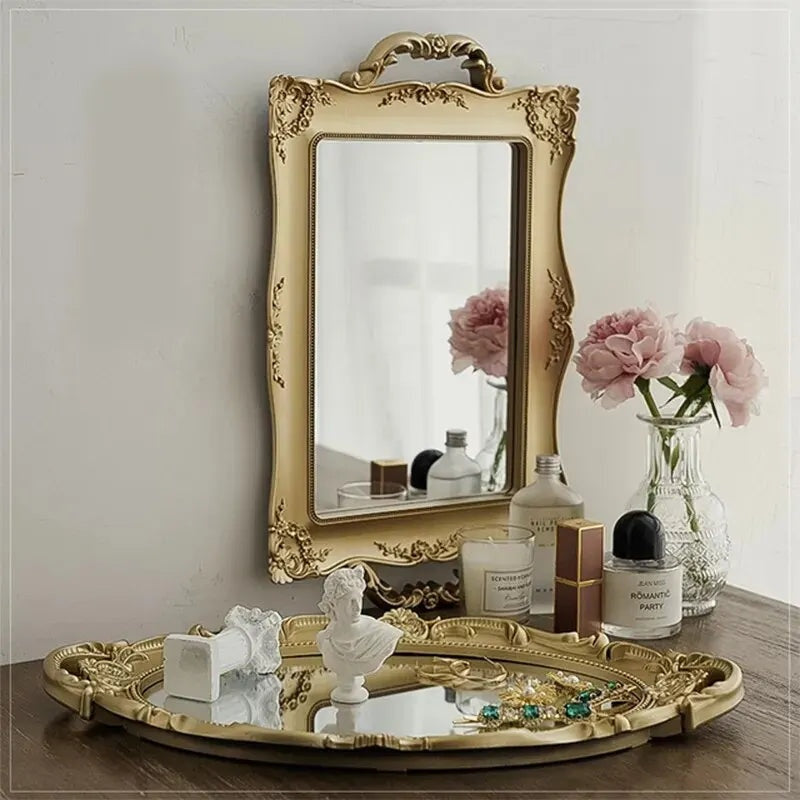 Plateau miroir ovale doré posé devant un miroir mural à cadre doré, avec fleurs et buste décoratif