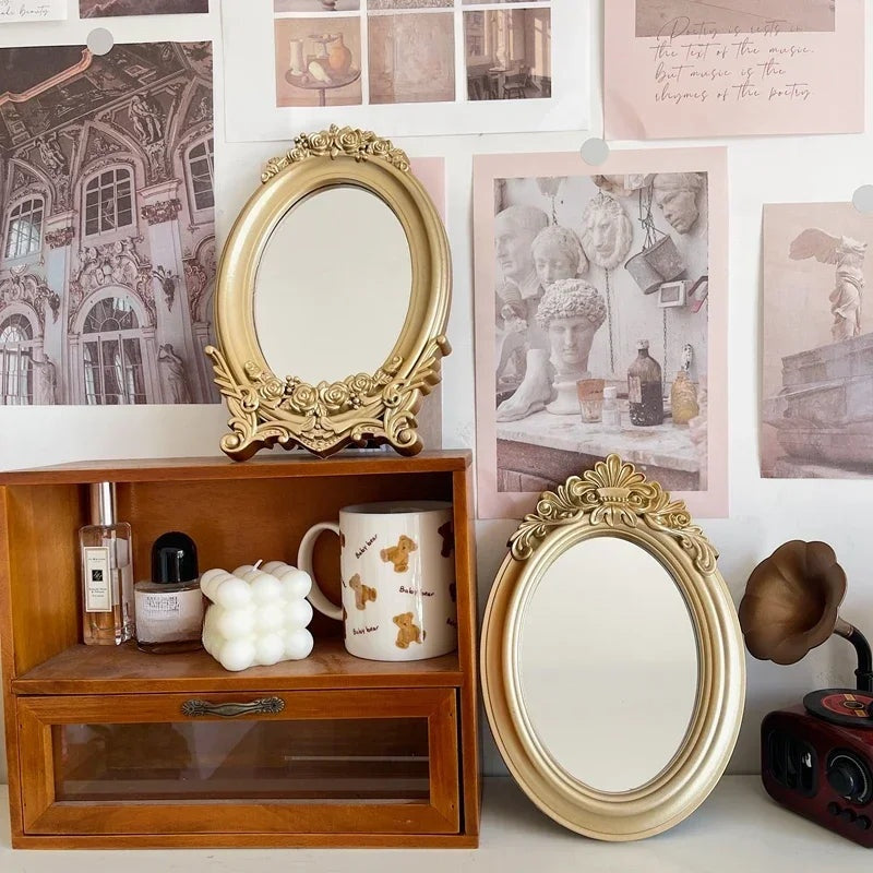 Deux miroirs de table ovales dorés posés sur et devant un meuble en bois, avec des photos au mur