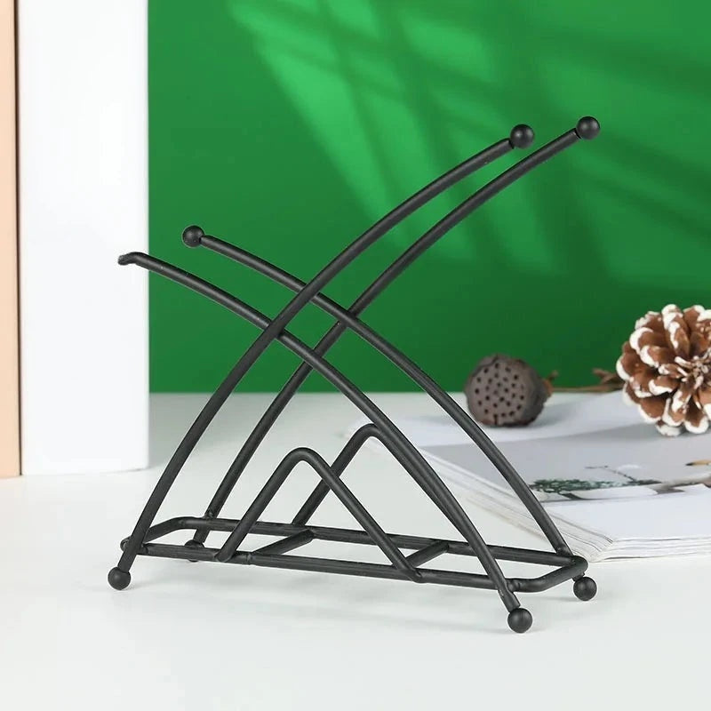 Porte-serviettes noir à branches croisées terminées par des boules, variante Noir Forme X, devant un fond vert