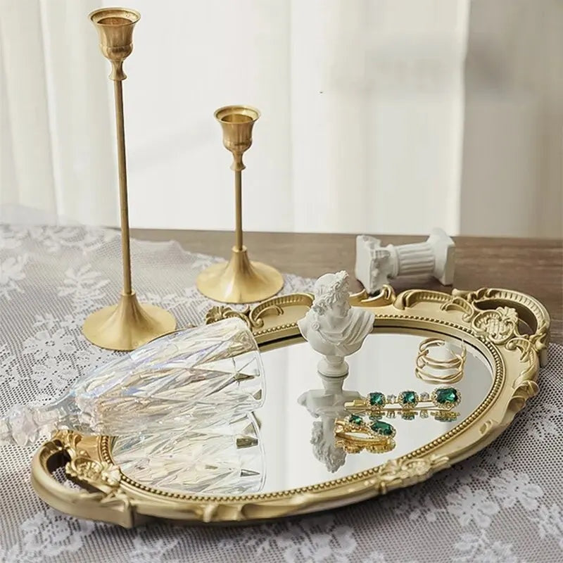 Plateau miroir ovale doré au cadre sculpté, avec bougeoirs dorés, verre et bijoux posés dessus