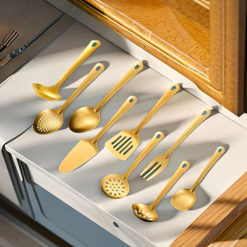 Ensemble d'ustensiles de service dorés en inox posés dans un tiroir : louches, cuillères, spatule et fourchette