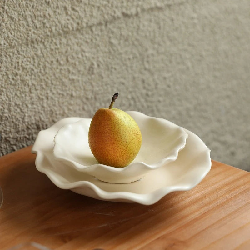 Trois plats en céramique crème à bord ondulé empilés, avec une poire dans le plus petit