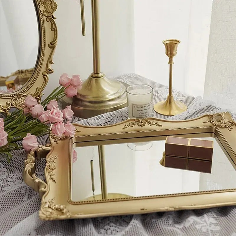 Plateau miroir rectangulaire doré portant un coffret, un bougeoir et des fleurs roses